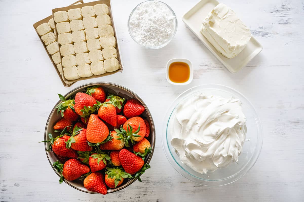 Strawberry Pizza Ingredients: A bowl of strawberries, whipped cream, cream cheese blocks, vanilla extract, powdered sugar, and refrigerated cookie dough.