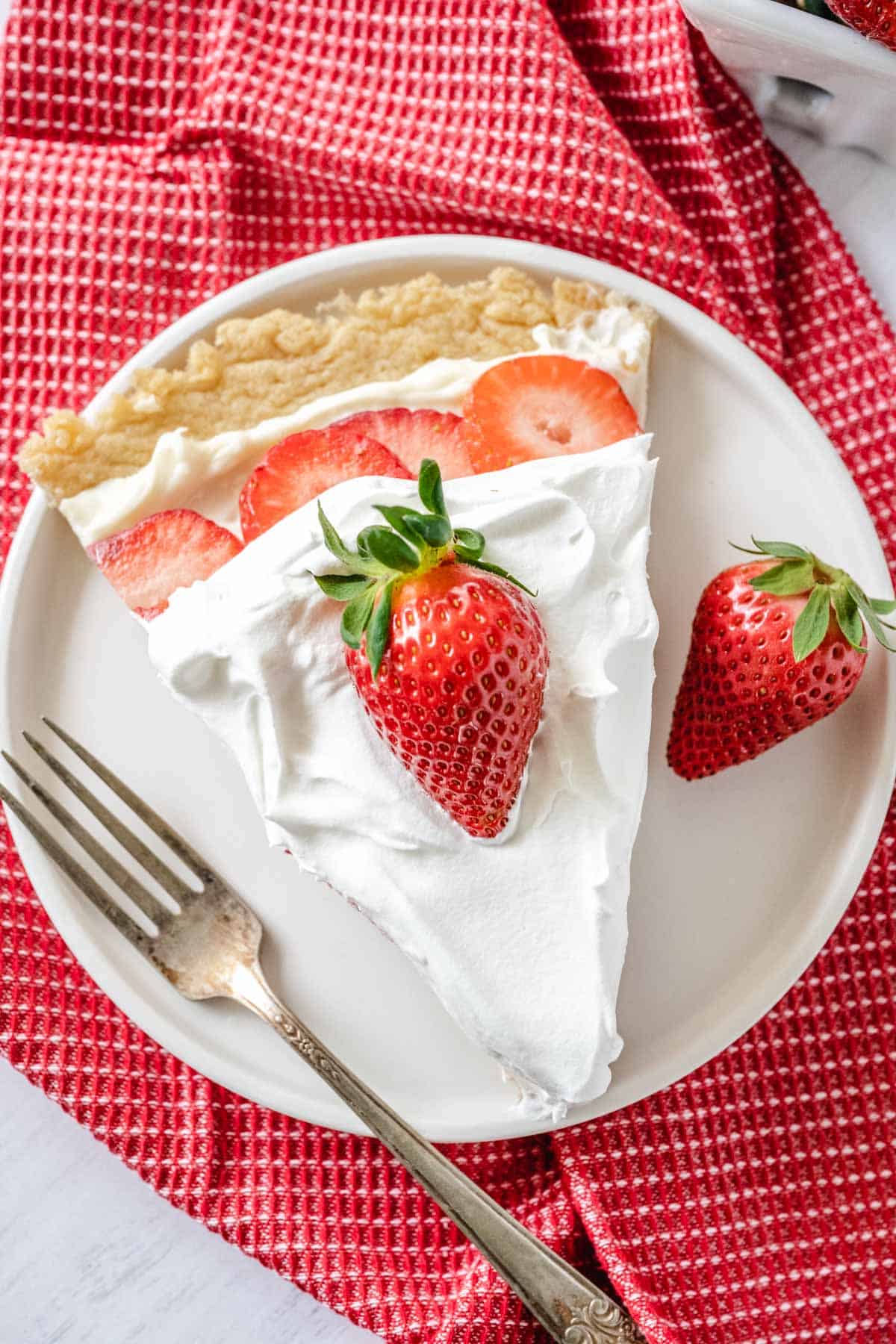 Slice of strawberry dessert on a white plate with a vintage fork beside the slice.