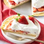 Slice of strawberry pizza plated with the whole pizza in the background.