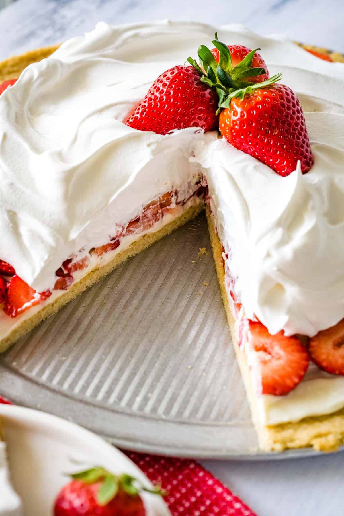 Whole strawberry pizza with a slice remove served on a silver pizza pan.