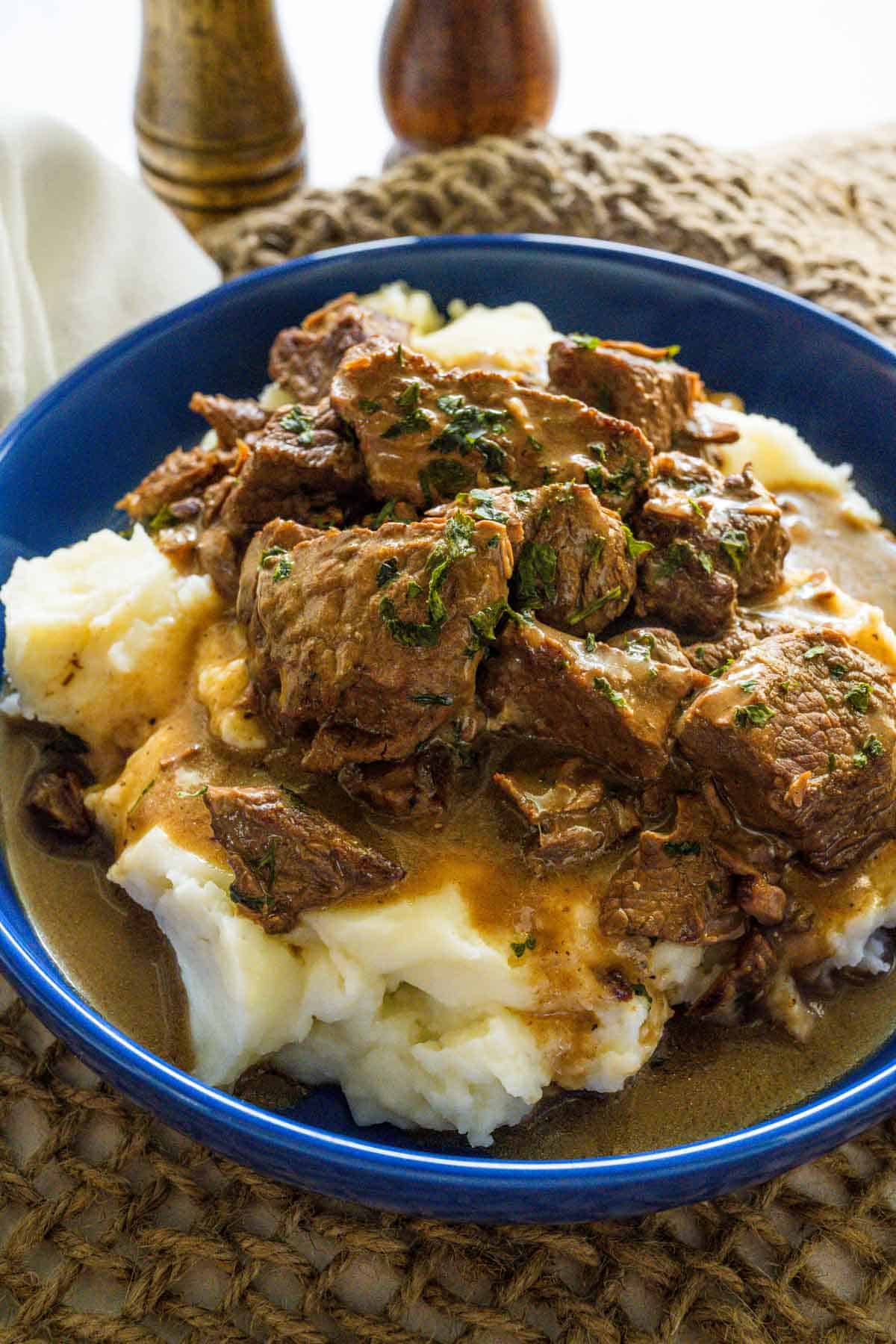 A bowl full of mashed potatoes topped with beef tips and gravy.