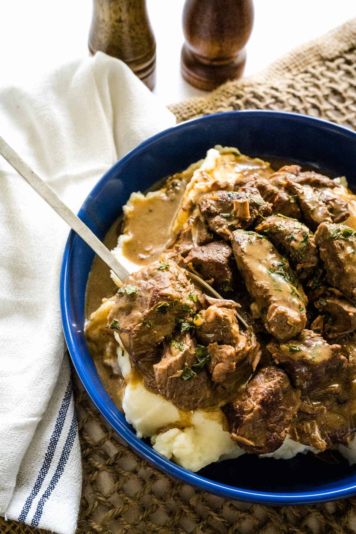 A blue bowl filled with beef tips, gravy, and mashed potatoes.