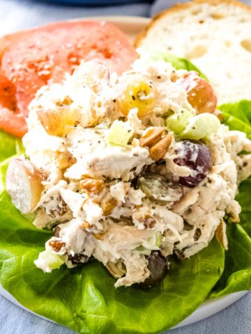 A scoop of the best chicken salad with grapes and pecans on a bed of lettuce.