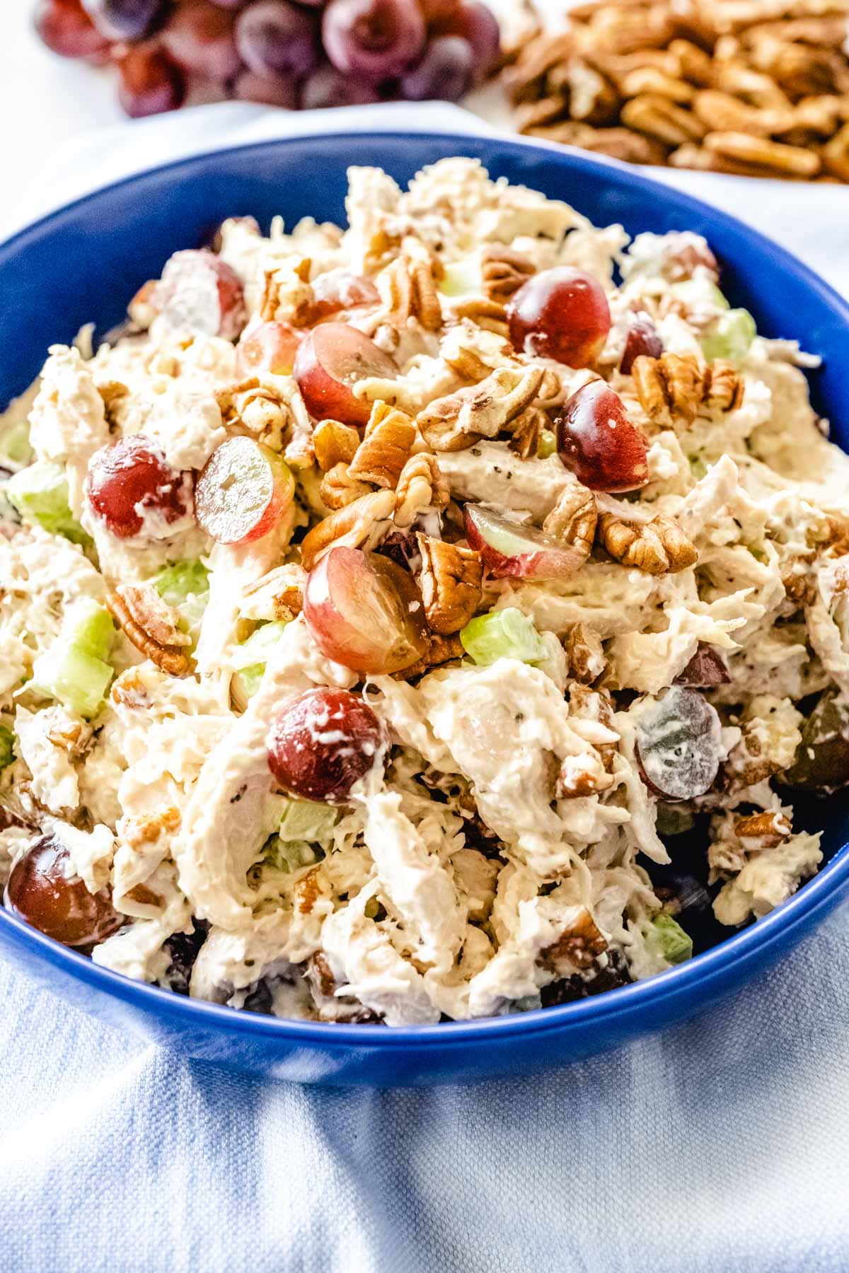 A bright blue bowl filled with chicken salad with grapes, pecans, celery tossed in mayo.