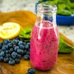 Blueberry Vinaigrette Dressing set on a wooden tray with blueberries, lemon, and greens in the background.