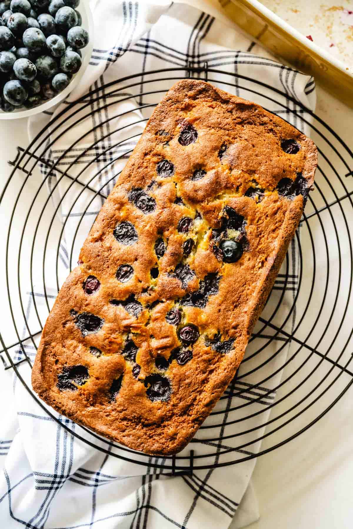 A loaf of blueberry banana bread on a round cooling rack.