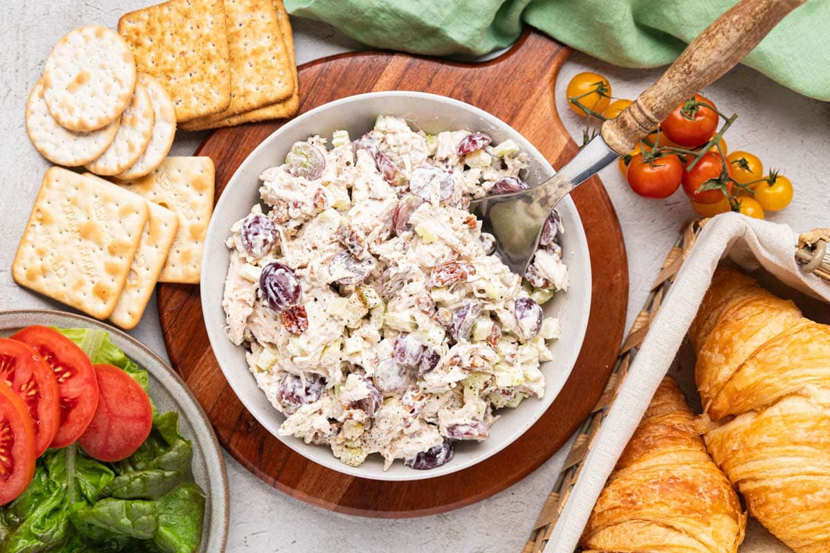Chicken salad with grapes and pecans in a white bowl set on a board with crackers.