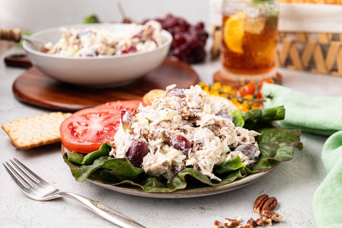 A scoop of southern chicken salad on a bed of lettuce with sliced tomatoes.