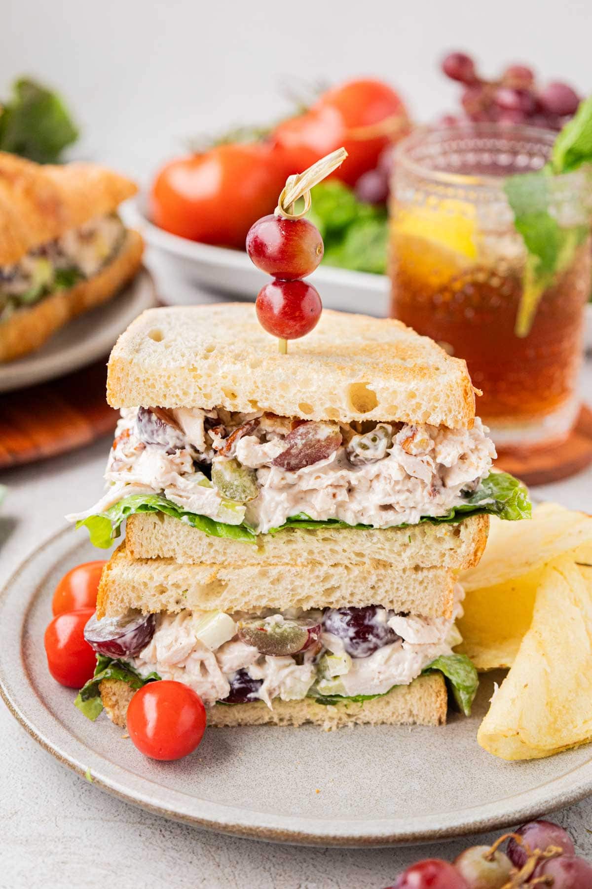 A chicken salad sandwich on toasted white bread stacked with a garnish toothpick with grapes on top.