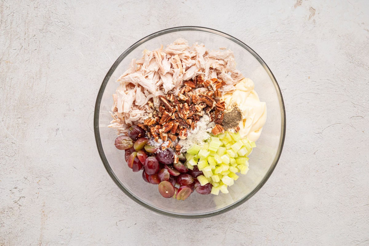 Chicken salad ingredients added to a glass bowl.