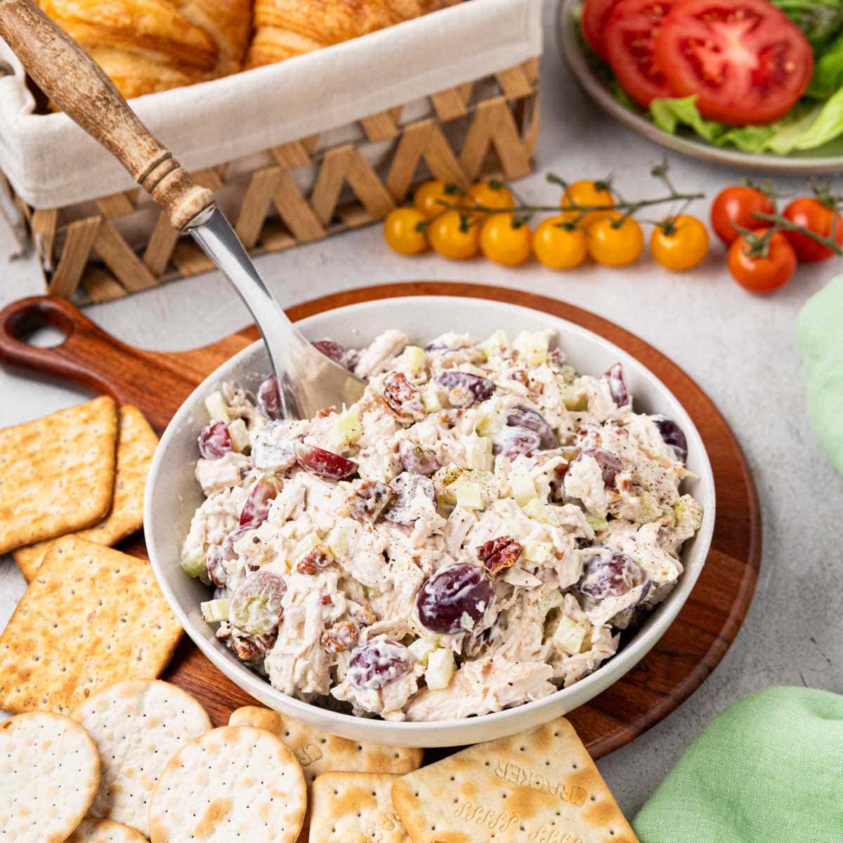 Chicken salad with grapes and pecans in a white bowl set on a board with crackers.