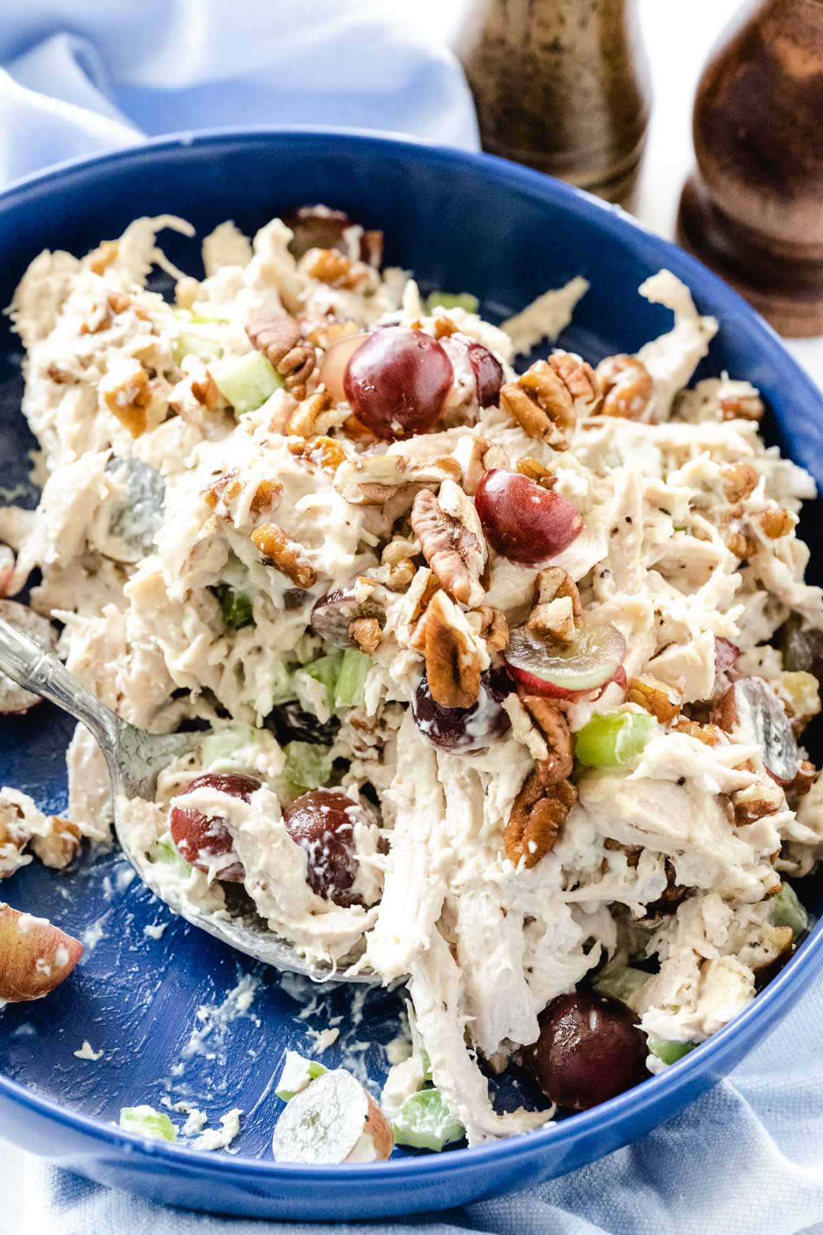 Chicken salad in a blue bowl with servings having been scooped out with a silver spoon.