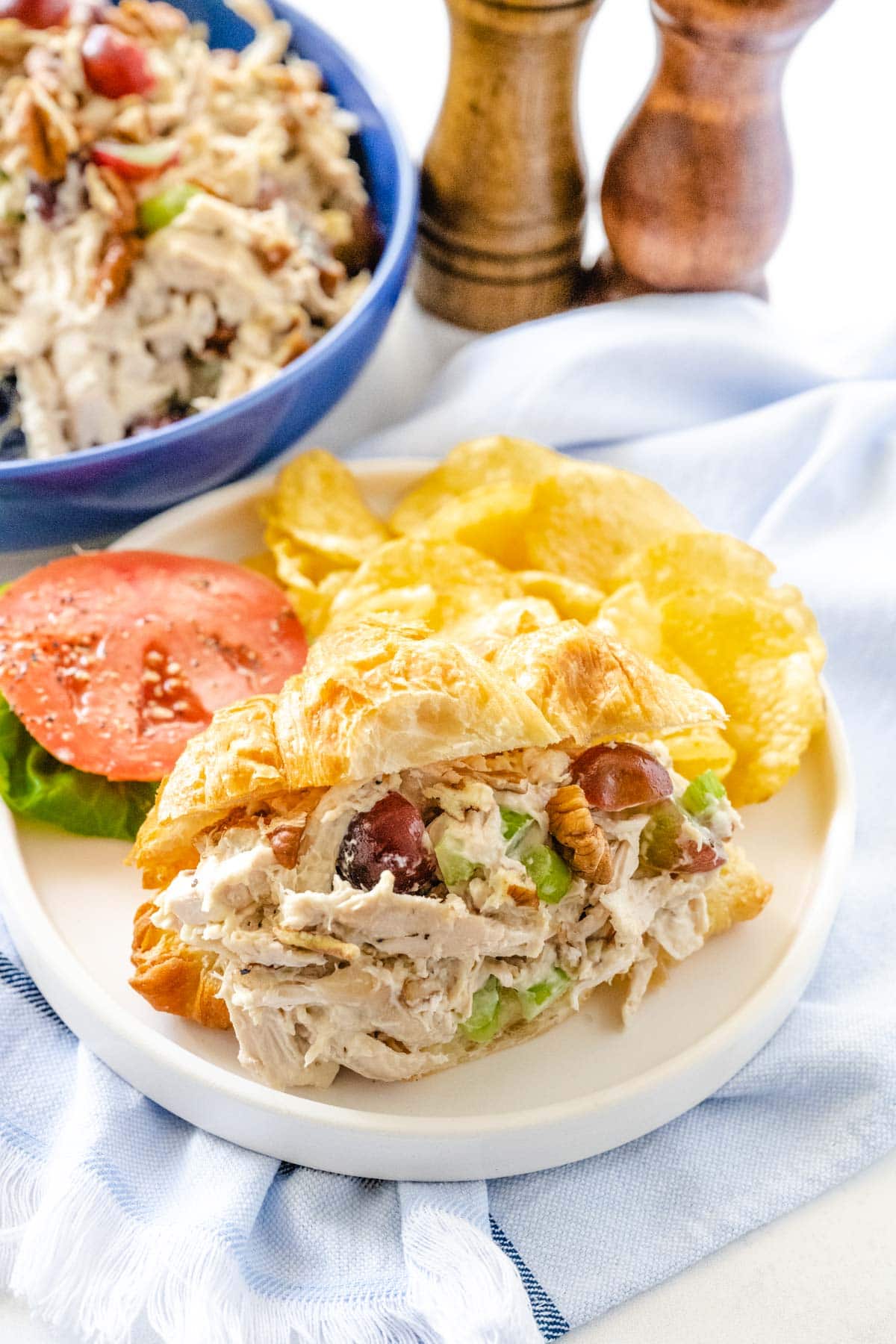 Chicken salad on a croissant plated with chips and lettuce and tomato. 