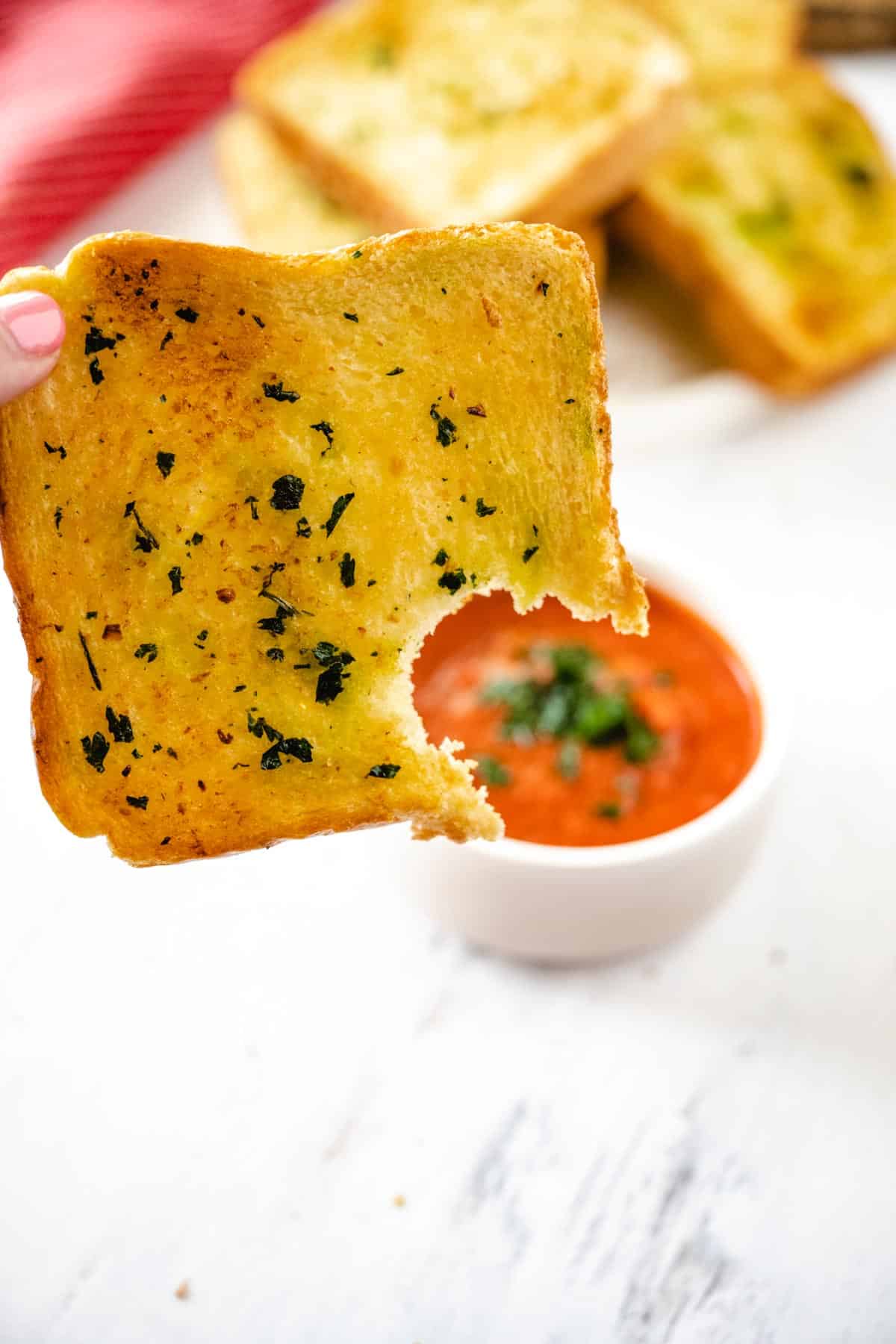 An upclose image of a slice of texas toast garlic bread with a bite taken out of it with a bowl of marinara sauce in the background.