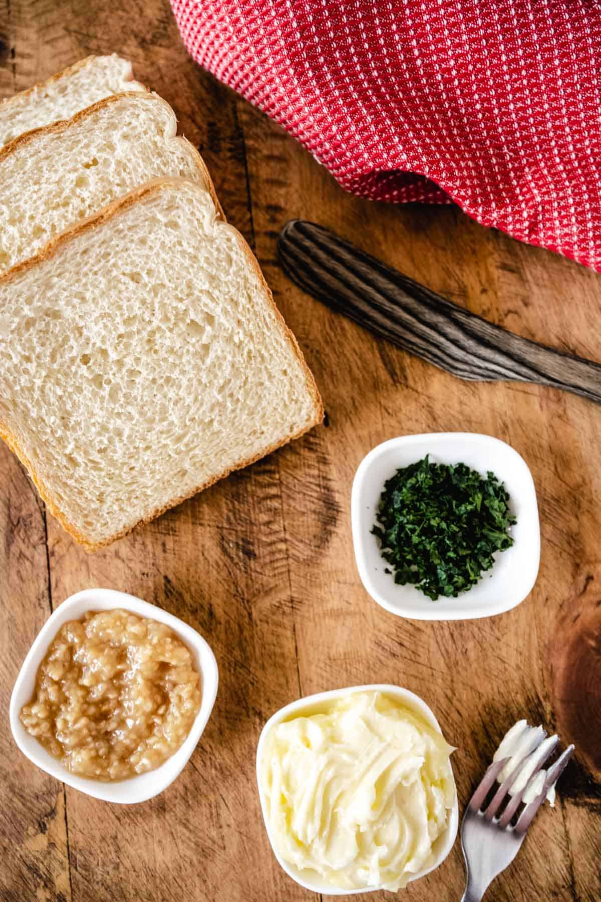 A wooden board filled with ingredients to make air fryer texas toast - thick sliced texas toast bread, minced garlic, butter, and chopped parsley.