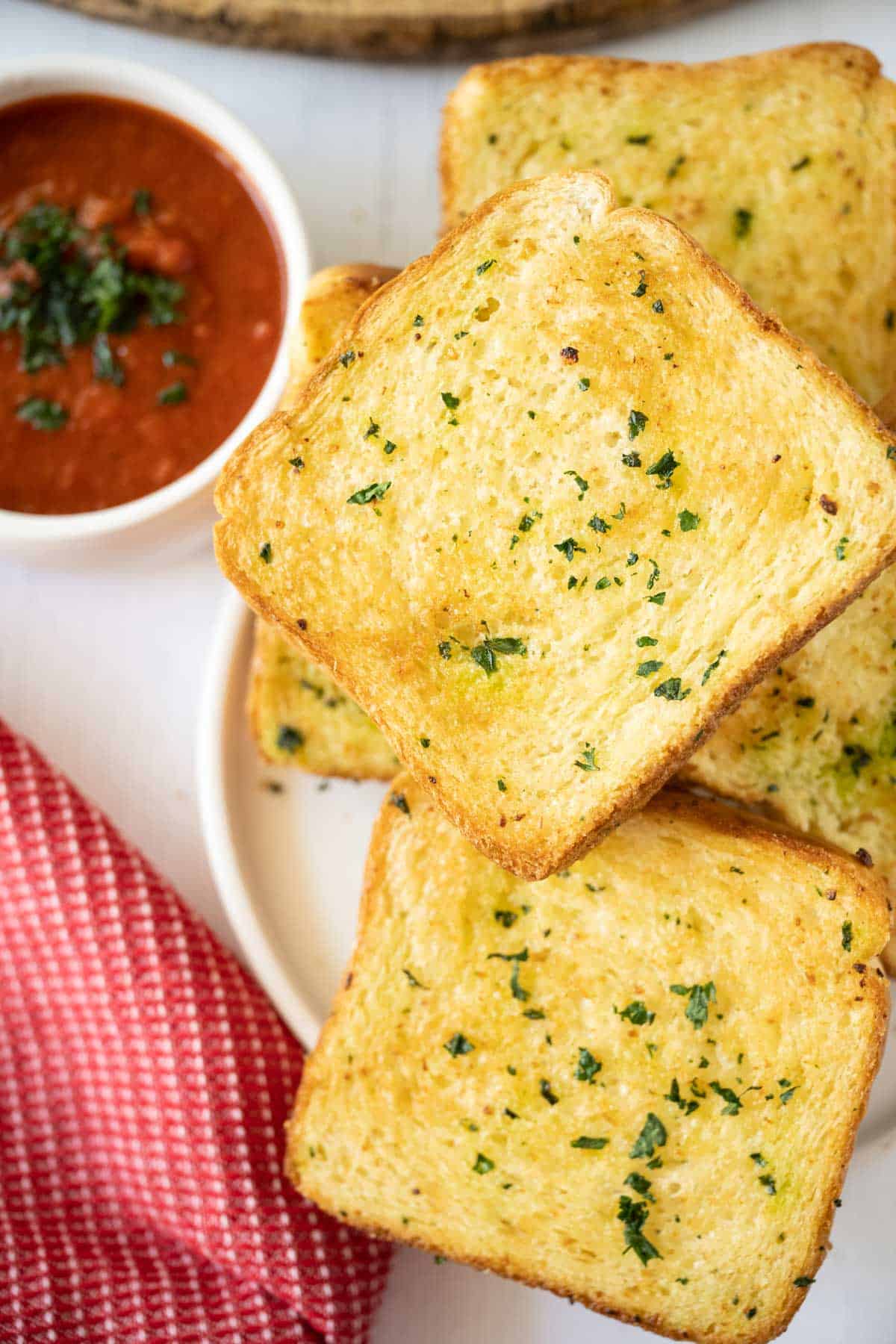 Slices of air fryer texas toast on a white plate with a bowl of marinara to the left of the plate.