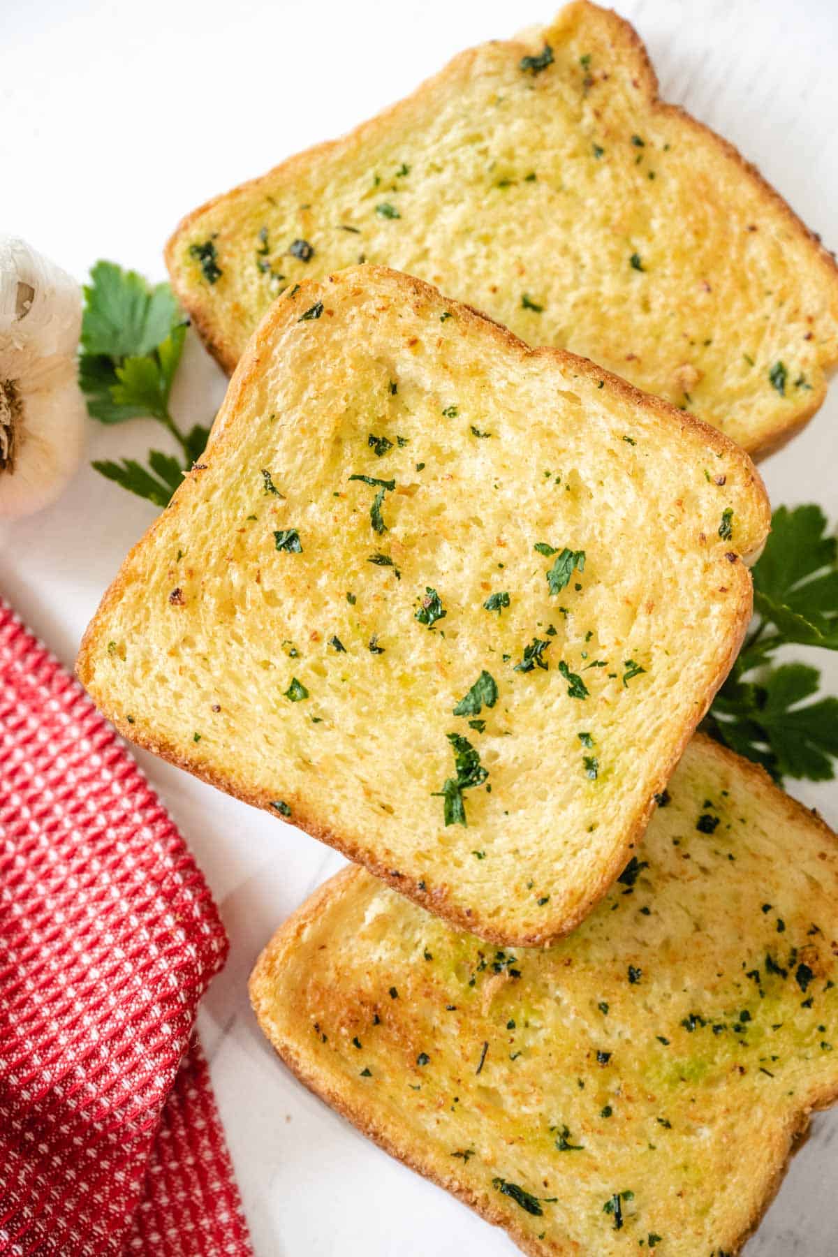 3 slices of air fryer texas toast garlic bread set on a white wooden board surrounded with garlic and parsley.