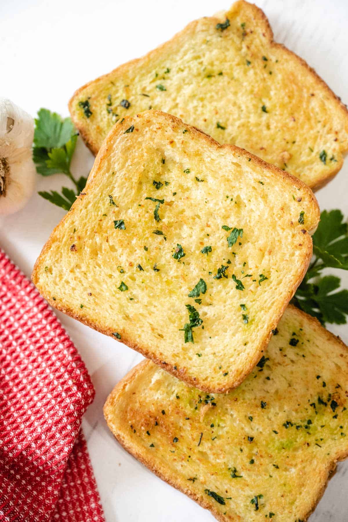 3 slices of air fryer texas toast garlic bread set on a white wooden board surrounded with garlic and parsley.