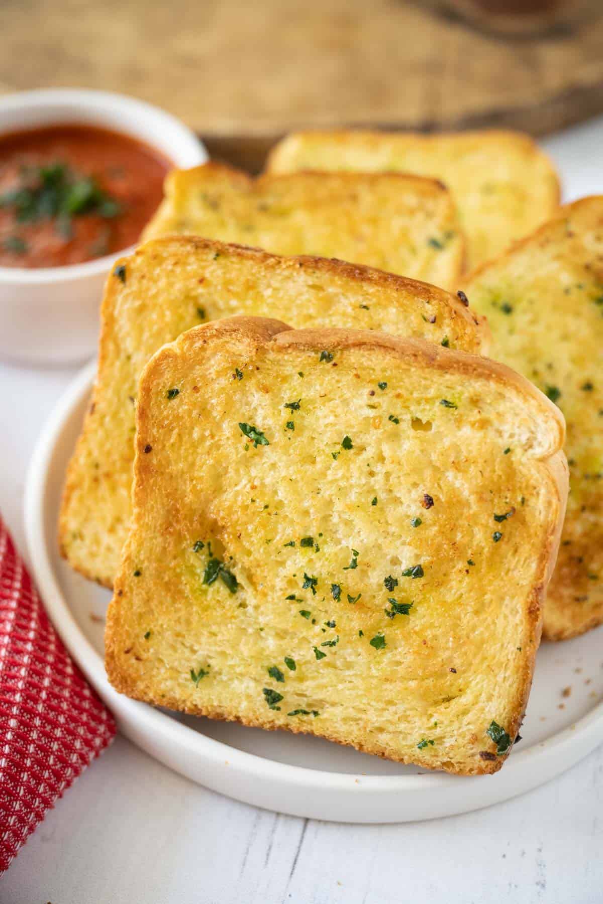 Slices of air fryer texas toast on a white plate stacked sideways showing the melted butter, garlic, and parsley on the garlic bread.