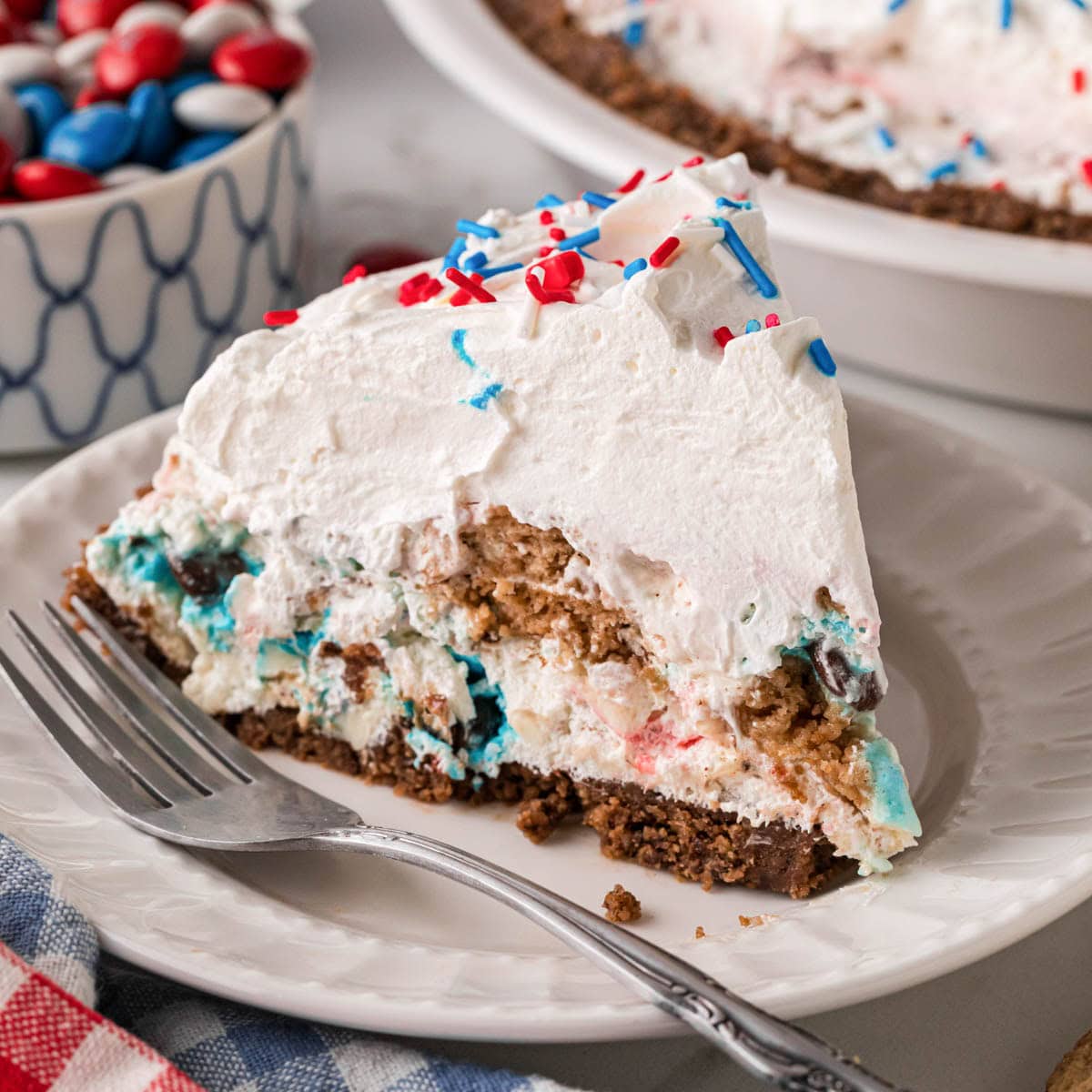 A slice of chocolate chip cookie candy cream pie on a plate with the pie in the background.