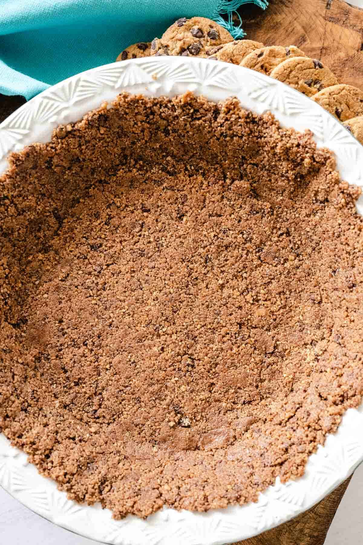 Upclose image of a chocolate chip cookie crust set on a wooden board with a blue tea towel and scatter chocolate chips cookies in the background.