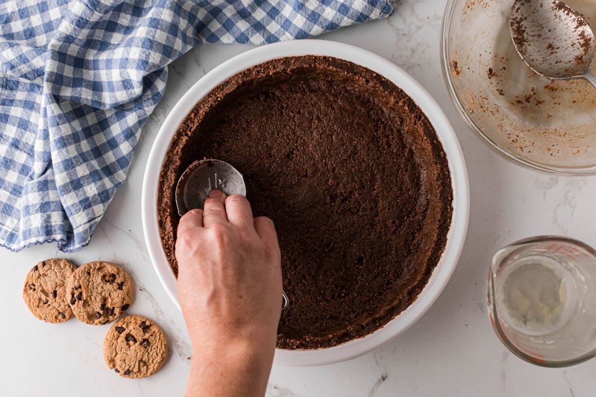 Pressing the cookie pie crust into the pie dish with a measuring cup.