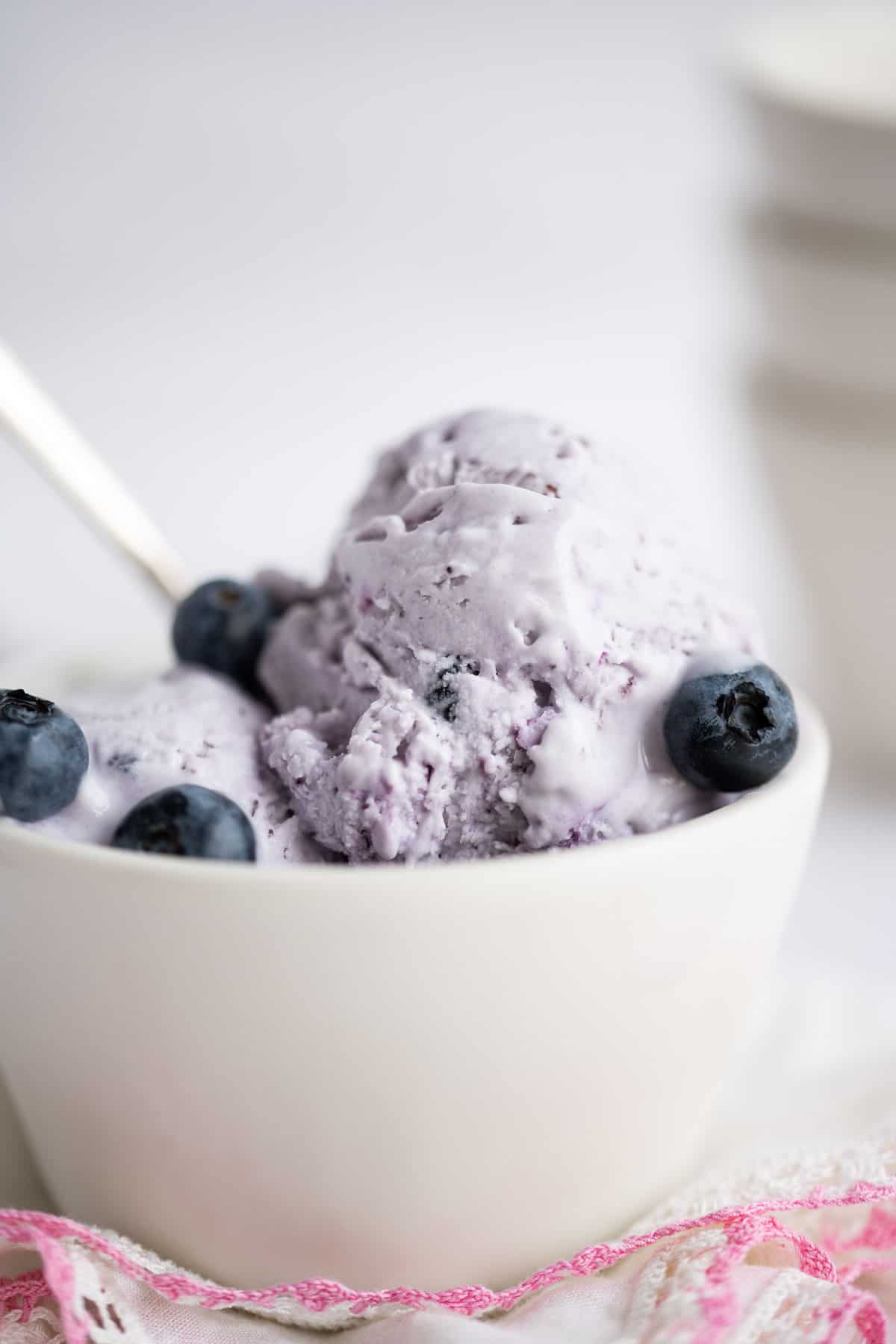 Blueberry ice cream in a blue bowl set on a white napkin trimmed in pink.