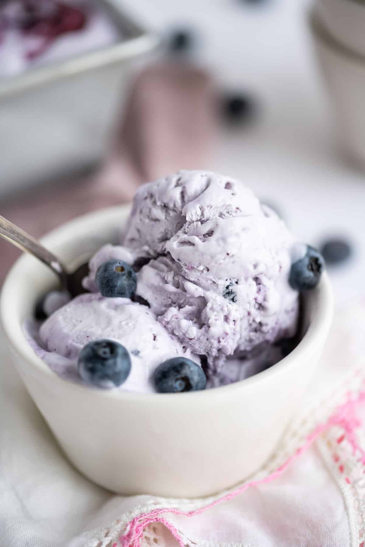 A bowl of no-church blueberry ice cream set in a white bowl garnished with blueberries.
