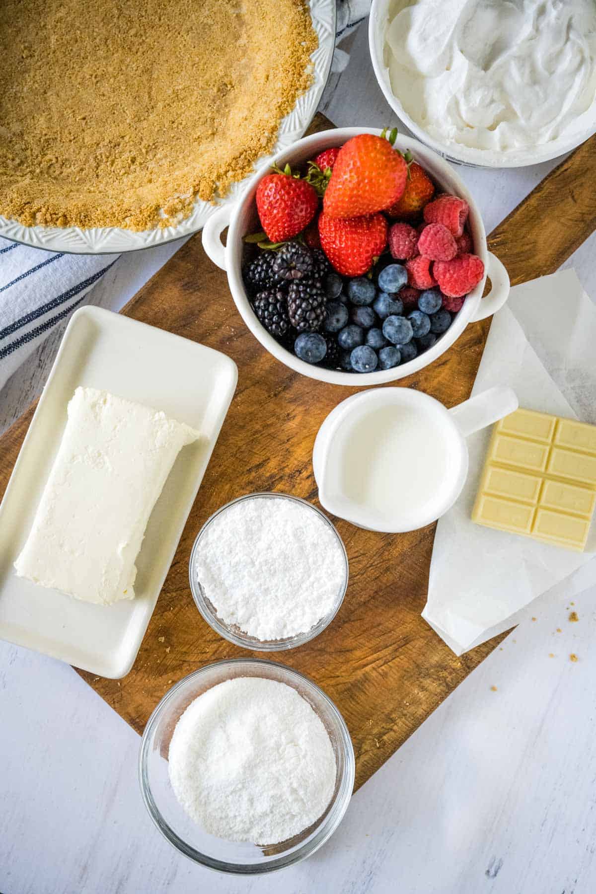 Ingredients needed for red white and blueberry cream pie on a wooden board.