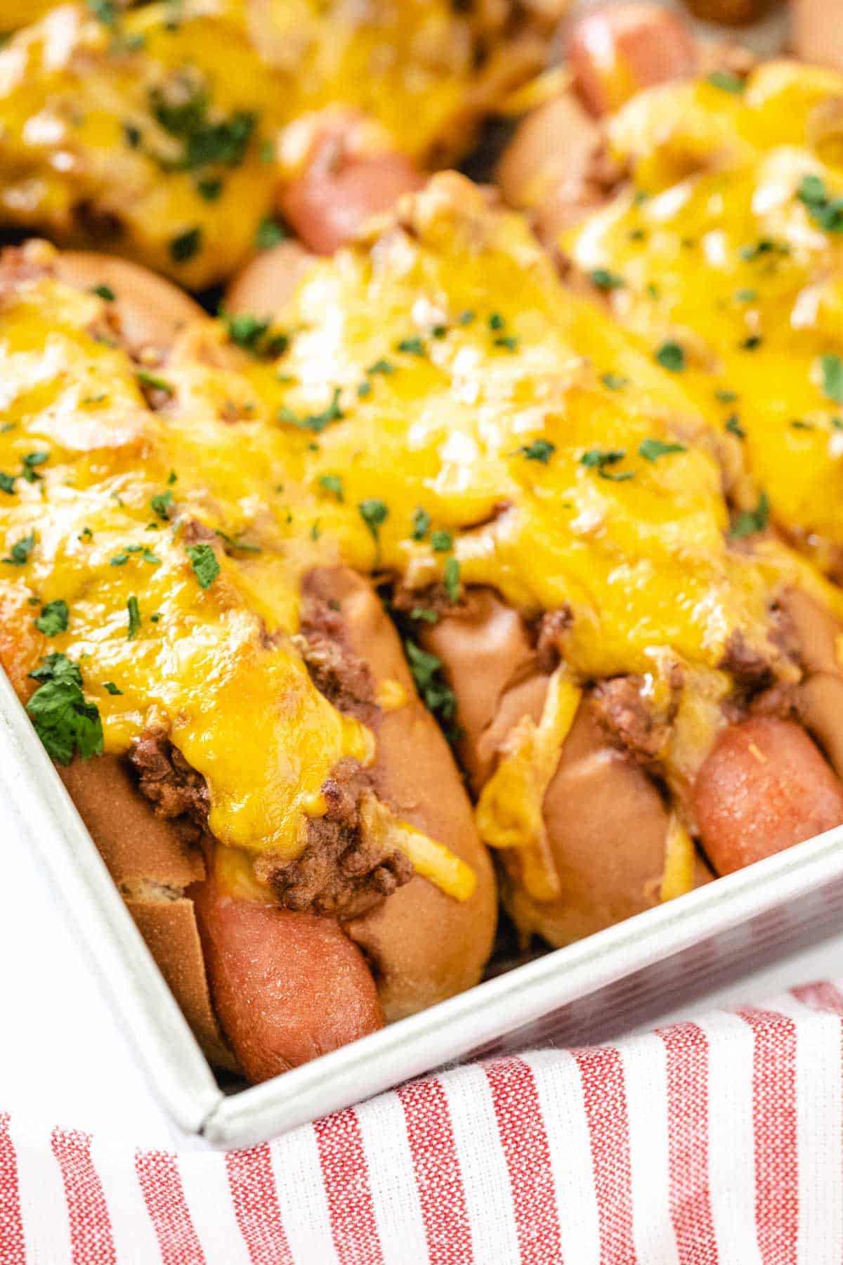 Hot dogs baked in a baking pan with chili and cheese on top.