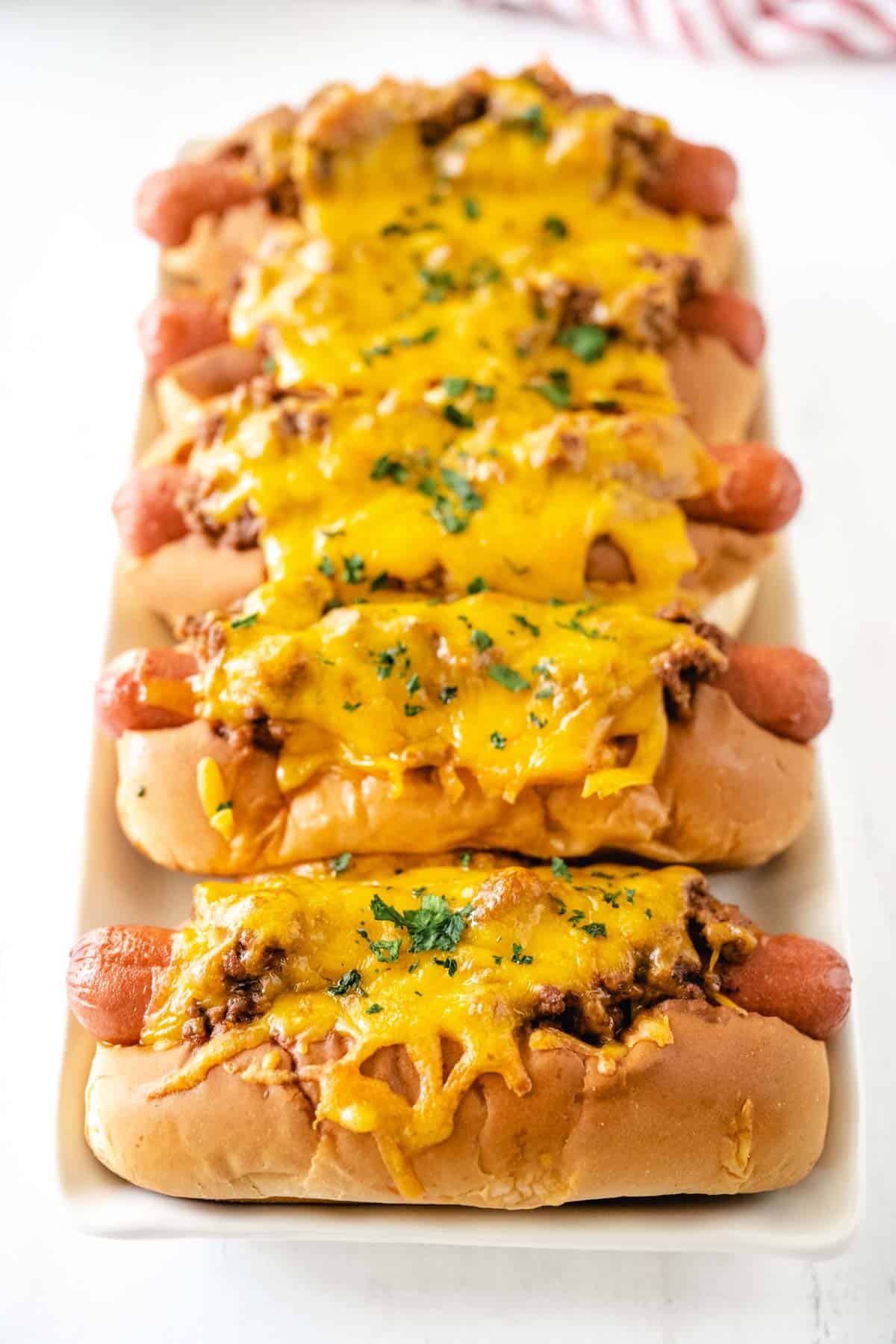 A white tray full of chili cheese dogs.