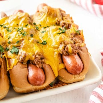 A white plate filled with baked chili cheese dogs.