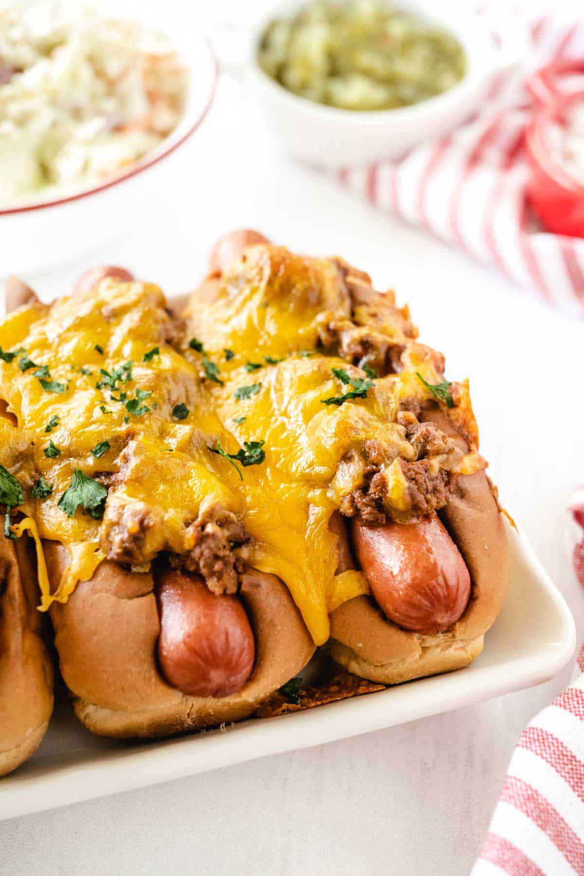 A plate of baked chili cheese dogs with a bowl of slaw and relish in the background.