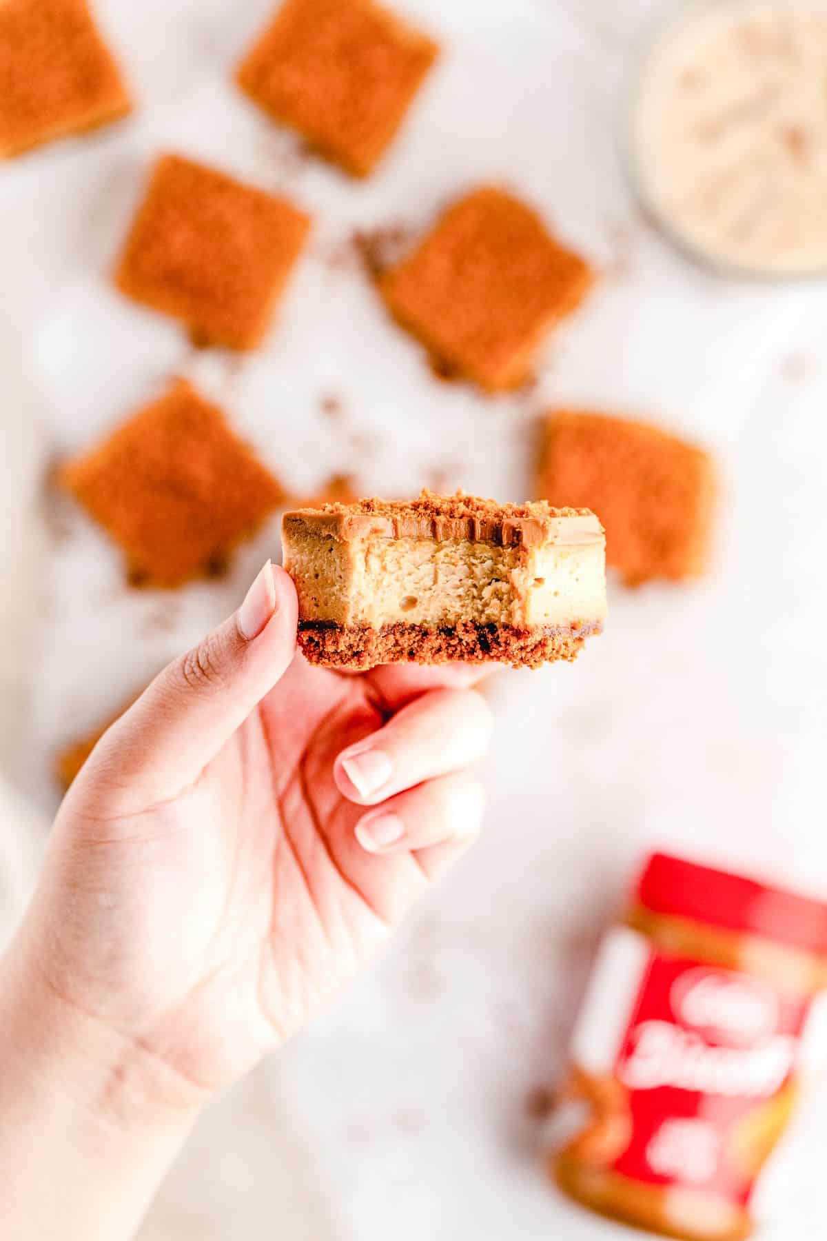 A hand holding a cheesecake bar with a bite taken out of the biscoff dessert bar.