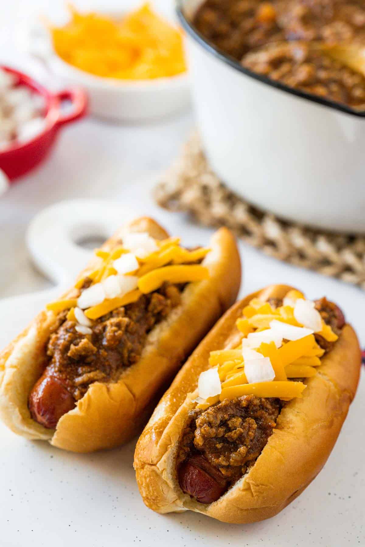 Two air fryer hot dogs topped with hot dog chili sauce, cheese, and diced onion.