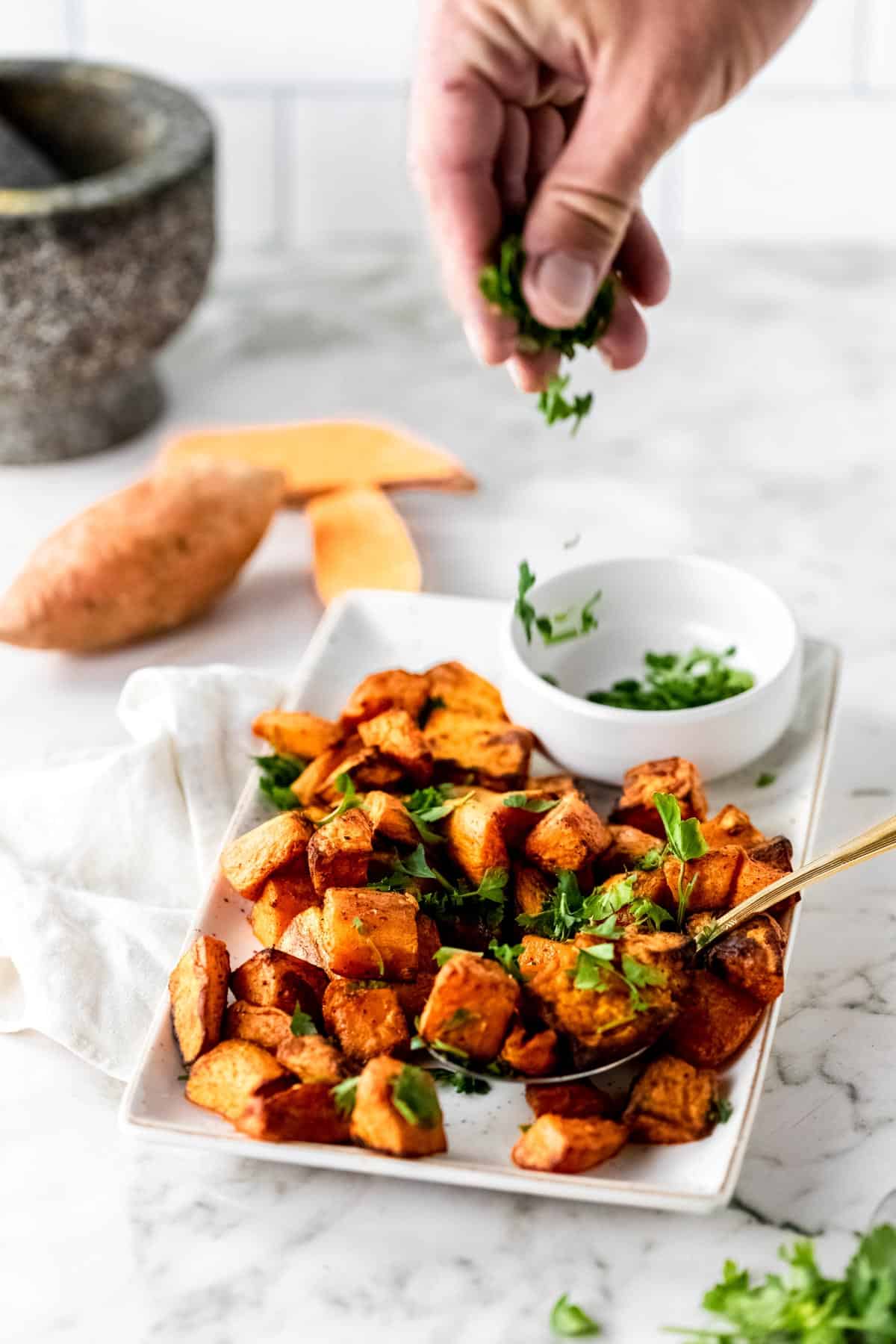 Sweet potato bites being sprinkled by hand with fresh cut parsley.