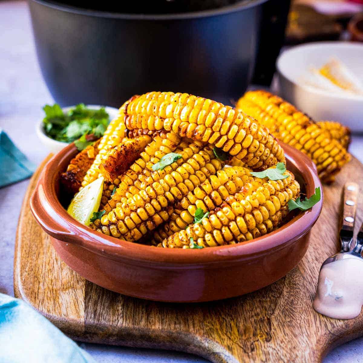 A bowl of corn ribs set on a wooden board with an air fryer bowl in the background.