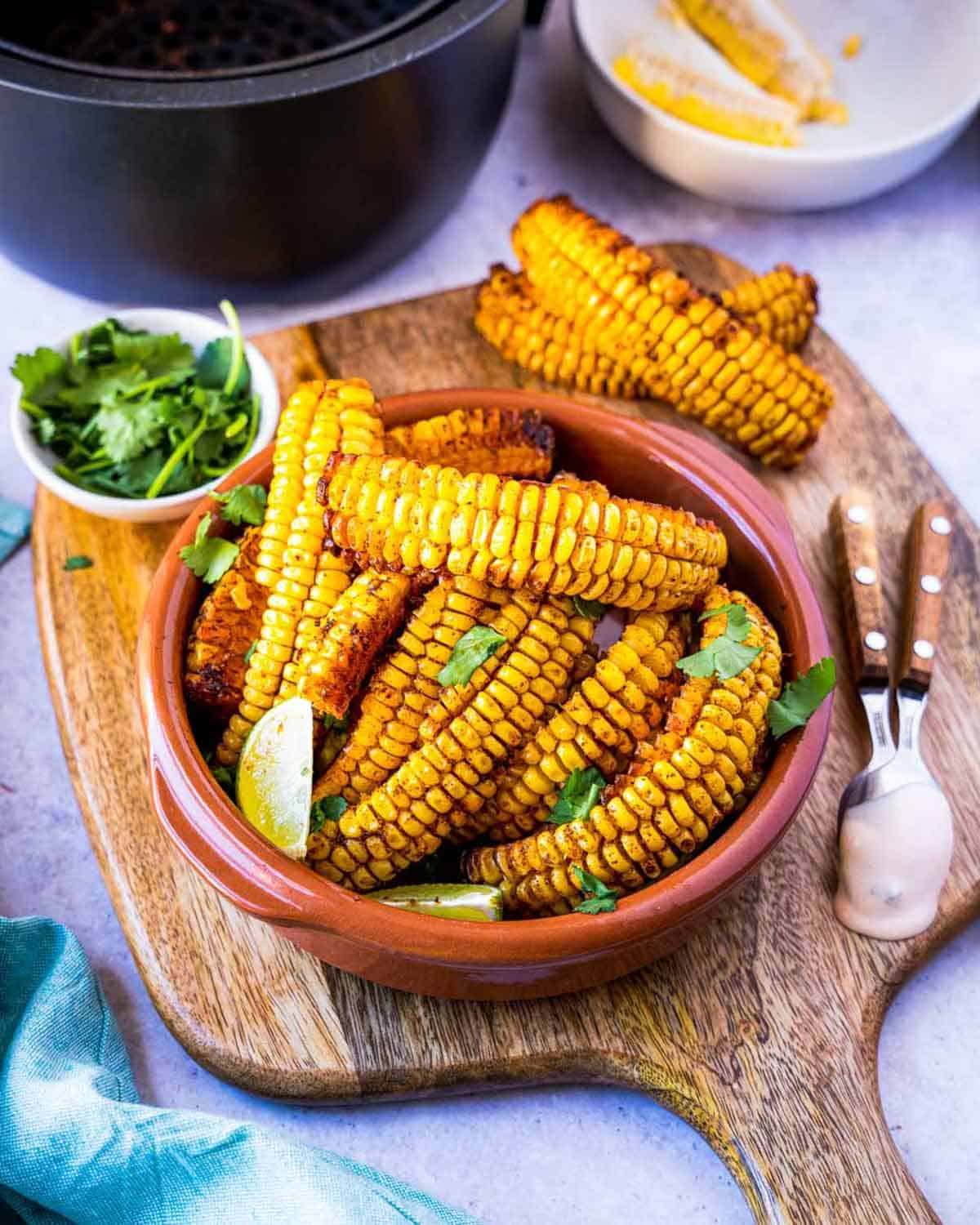 Corn Ribs set on a wooden tray in a terracotta colored bowl garnished with lime and cilantro.