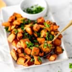 Air fryer sweet potato bites tossed with olive oil, cinnamon, and brown sugar set on a white plate served with parsley garnish.