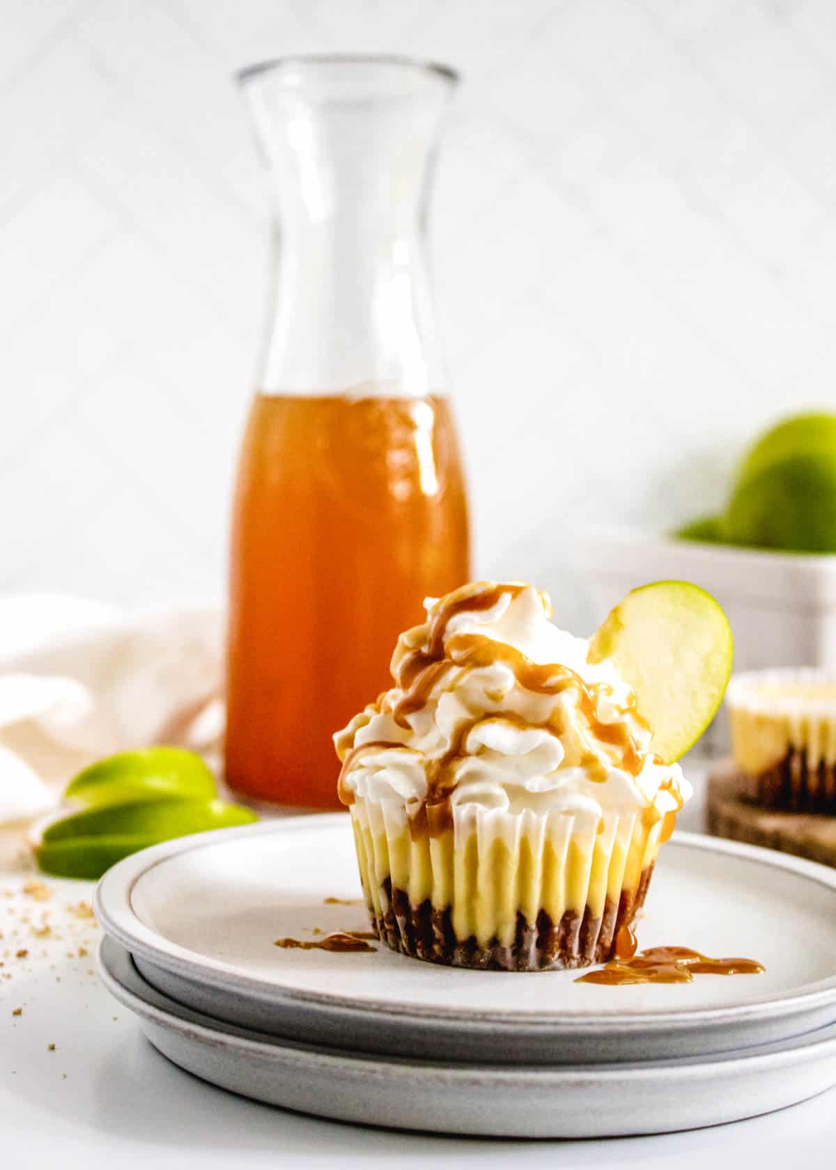 A plate with a mini caramel apple cheesecake with sliced apples and a jar of caramel in the background.