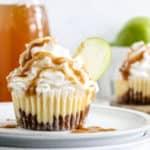 A caramel apple mini cheesecake topped with whipped cream and a caramel drizzle on a plate.