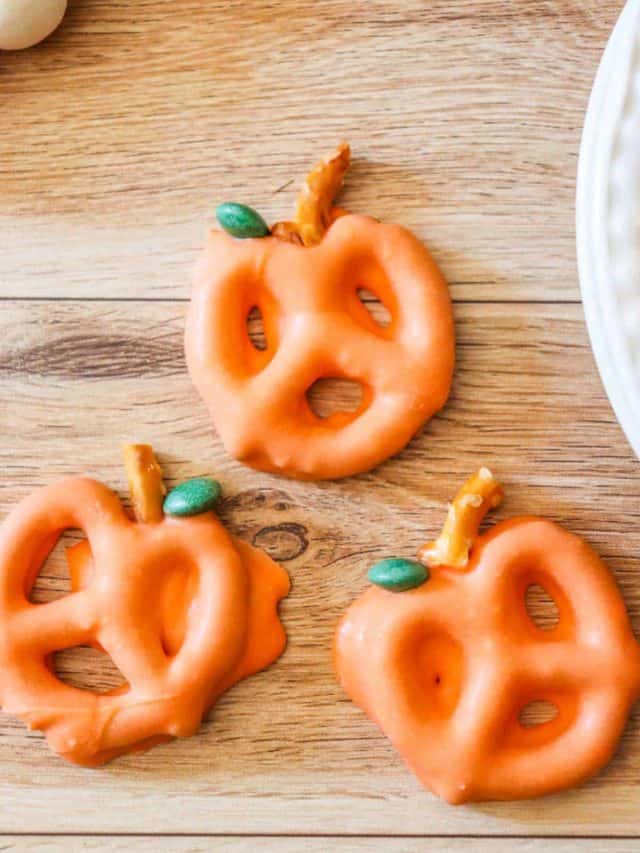 Three chocolate covered pretzels shaped like pumpkins on a wooden tray.
