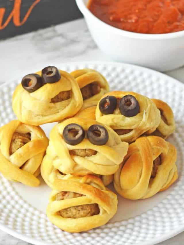 Meatballs wrapped like mummies with olive eyes on a white plate.