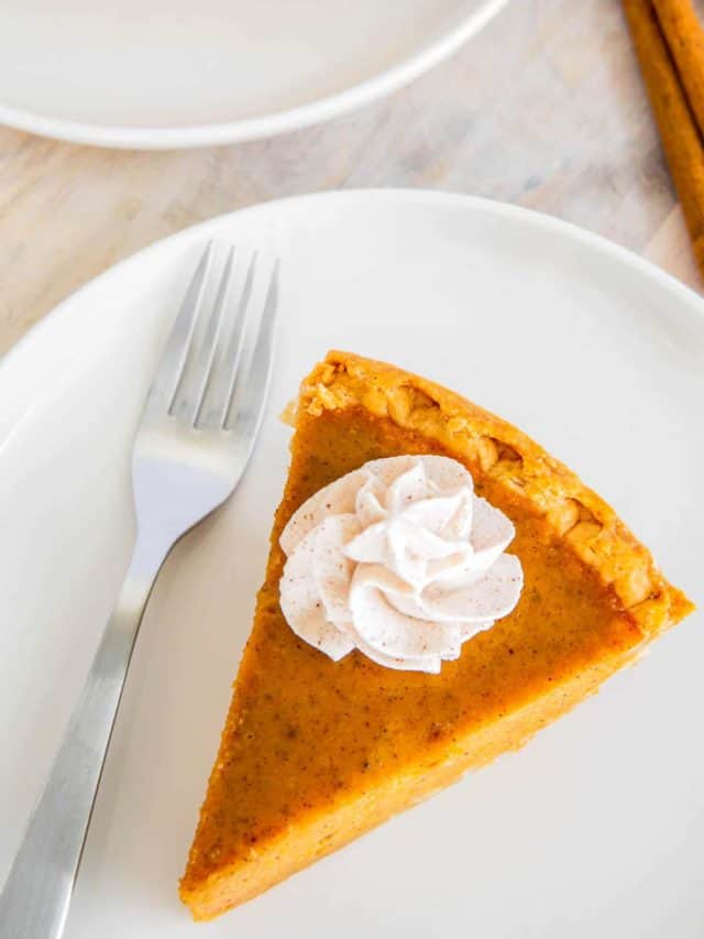 A pumpkin pie slice on a white plate with a fork to the side.