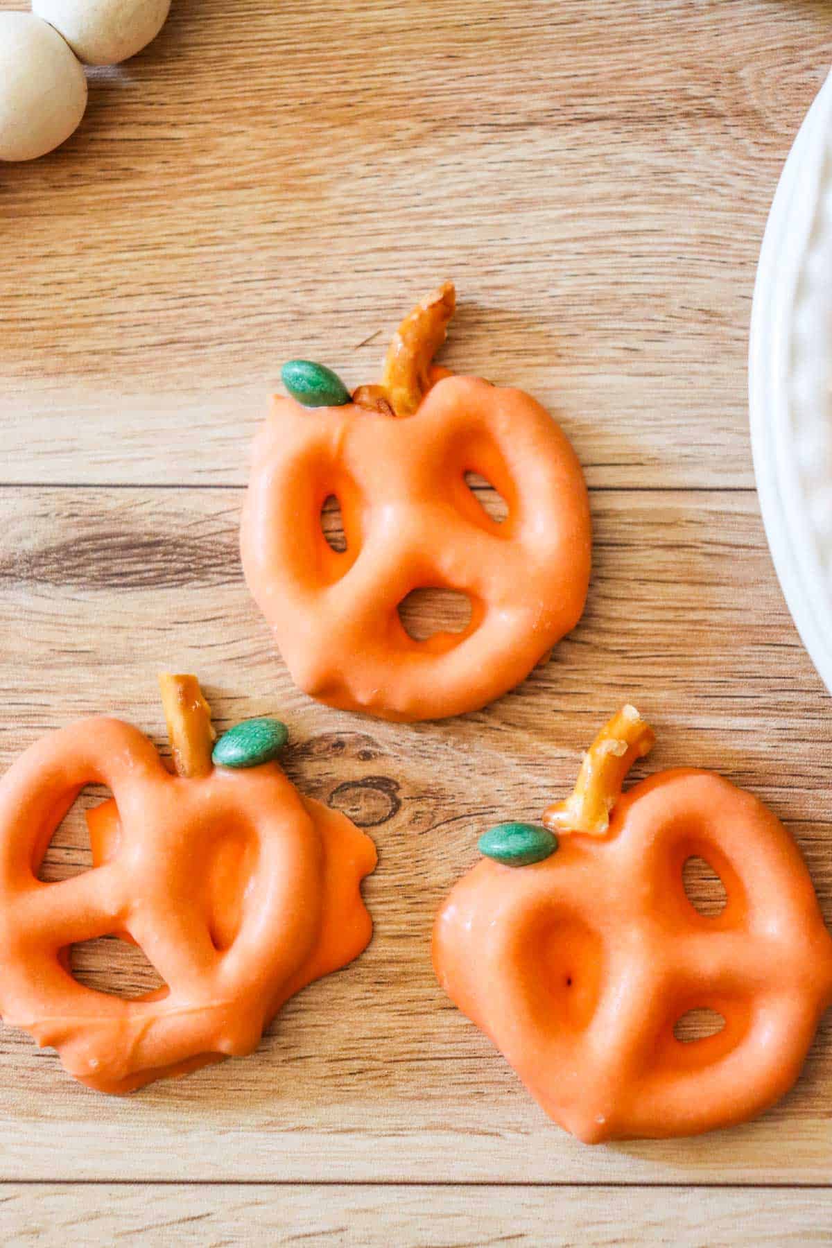 Three chocolate covered pretzels shaped like pumpkins on a wooden tray.