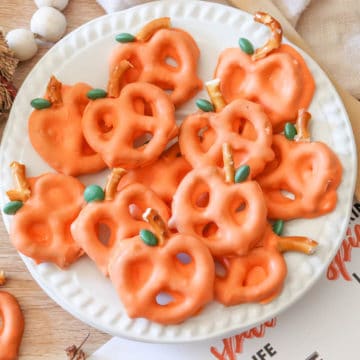 A white plate full of pretzels covered in orange colored chocolate decorated to look like a pumpkin.