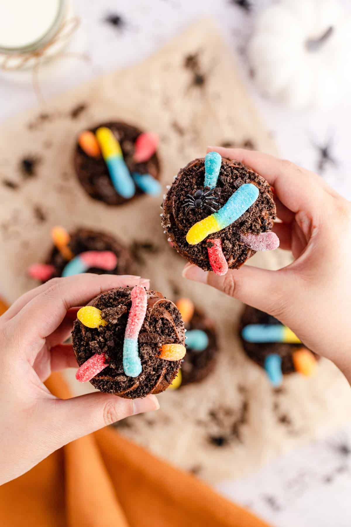 Two gummy worm dirt cupcakes held up by hands showing the overhead view of the cupcake.