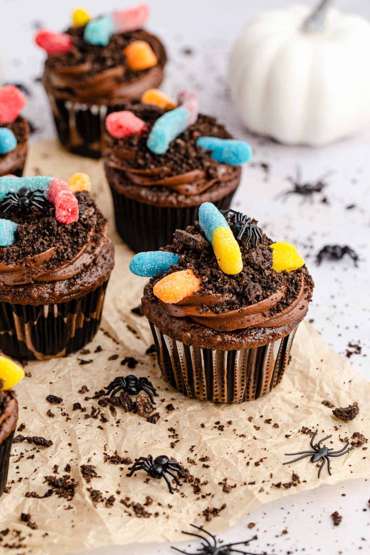Gummy worm dirt cupcakes with a white pumpkin in the background.