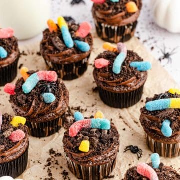 Upclose image of batch of chocolate cupcakes topped with homemade chocolate frosting, Oreo cookie crumbs, and sour gummy worms.