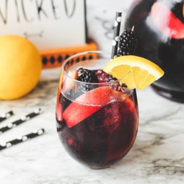 A glass of sangria on a marble table with a cute halloween polka dot straw and fruit in the glass.